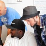 Drei Männer schauen gemeinsam auf einen Tisch.